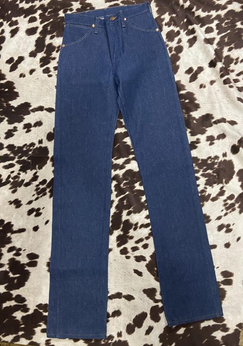 May include: A pair of classic blue denim jeans. The jeans have a straight leg cut, a button and zipper closure, and classic five-pocket styling. The jeans are displayed on a cowhide patterned surface.