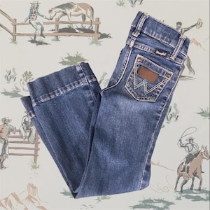 Op de afbeelding: Een donkerblauwe spijkerbroek van denim met een klassiek ontwerp met vijf zakken, een Wrangler-merklabel op de achterzak, koperkleurige klinknagels en decoratieve stiksels op de achterzakken. De broek heeft een rechte snit en een medium wassing.
