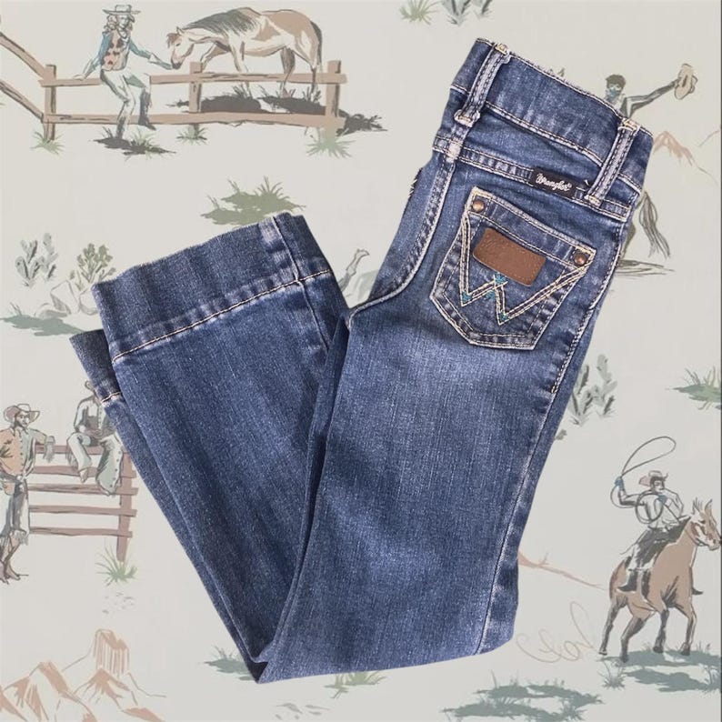 Op de afbeelding: Een donkerblauwe spijkerbroek van denim met een klassiek ontwerp met vijf zakken, een Wrangler-merklabel op de achterzak, koperkleurige klinknagels en decoratieve stiksels op de achterzakken. De broek heeft een rechte snit en een medium wassing.