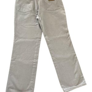 Op de afbeelding: Lichtgrijze denim jeans met een klassiek ontwerp met vijf zakken. De jeans hebben een bruine leren patch op de achterzak en een metalen knoopsluiting. Het merk Wrangler is zichtbaar.