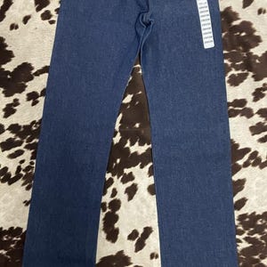 May include: Dark blue denim jeans with the Wrangler logo on the back pockets and a leather patch. The jeans have a classic five-pocket design and a straight leg. The tag shows the size.