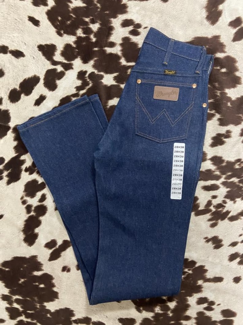 May include: Dark blue denim Wrangler jeans with a brown leather patch and the Wrangler logo on the back pocket. The jeans have a classic five-pocket design and a straight leg. The size tag shows a 28x38 size.