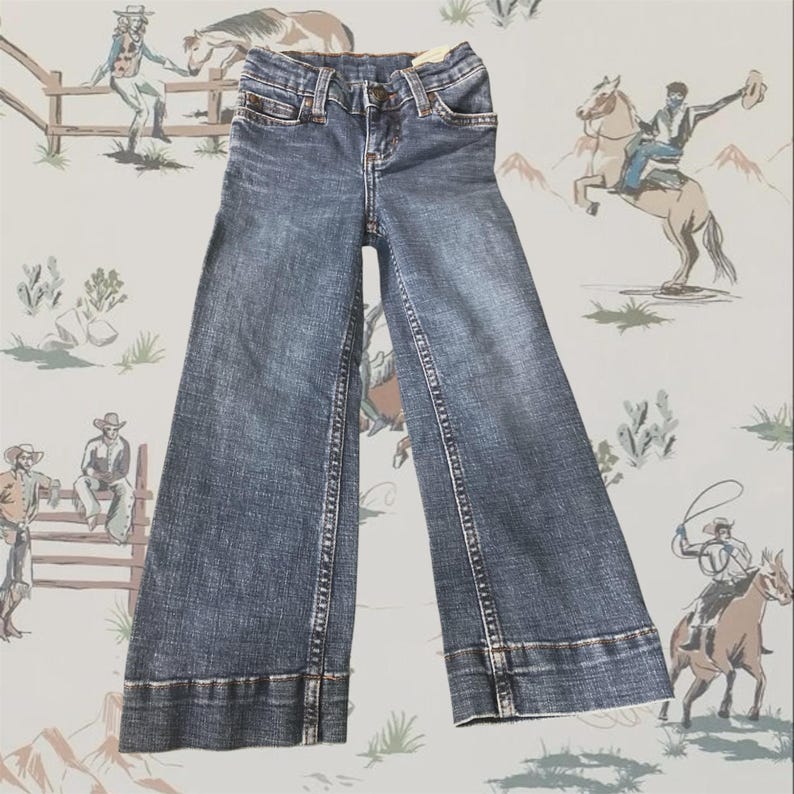 May include: A pair of medium-wash blue denim jeans featuring a wide-leg silhouette, a classic five-pocket design, a button and zipper fly closure, and visible copper-toned stitching along the seams and the wide hem at the bottom of the legs.