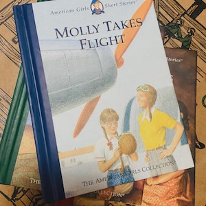 May include: A stack of children's books from "The American Girls Collection." The top book, "Molly Takes Flight," features a cover illustration of two girls and an airplane. The books have colorful covers and are set against a patterned background.