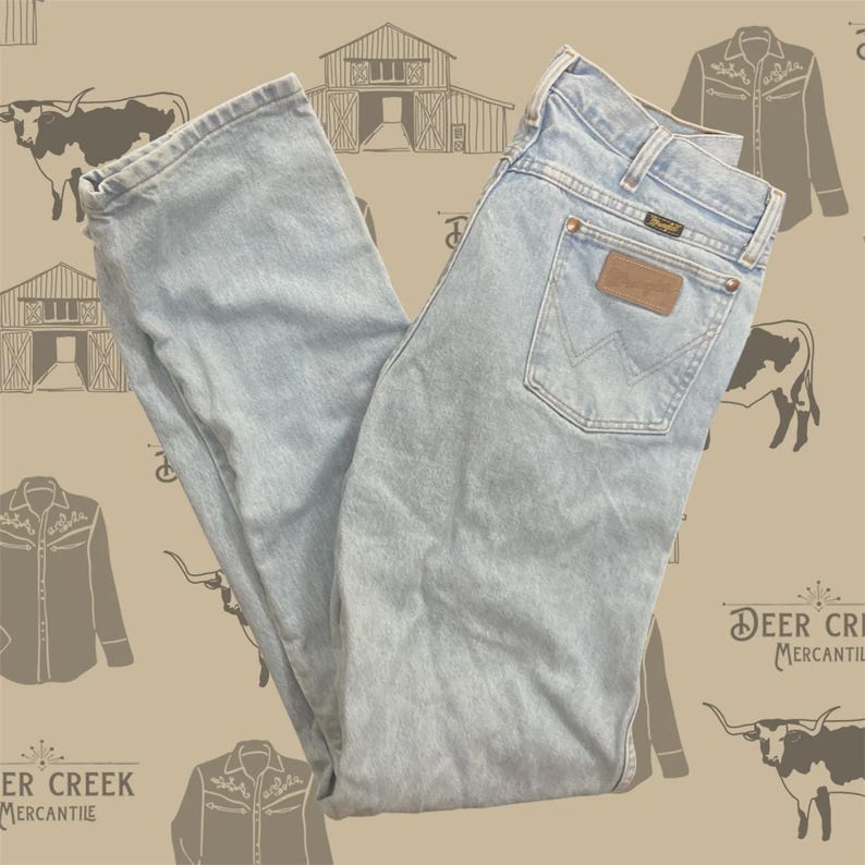 Pu&ograve; includere: Jeans in denim azzurro con taglio a gamba dritta, design classico a cinque tasche, etichetta in pelle marrone sulla tasca posteriore con logo Wrangler, rivetti color rame e una caratteristica cucitura a forma di W sulla tasca posteriore.