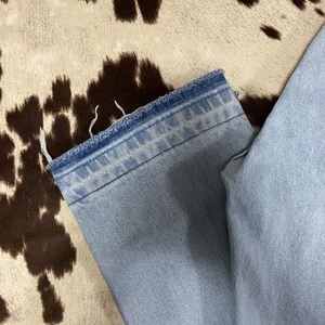 May include: Light blue denim jeans with a frayed hem. The jeans are a light wash. The background is a cowhide pattern in shades of brown and cream.