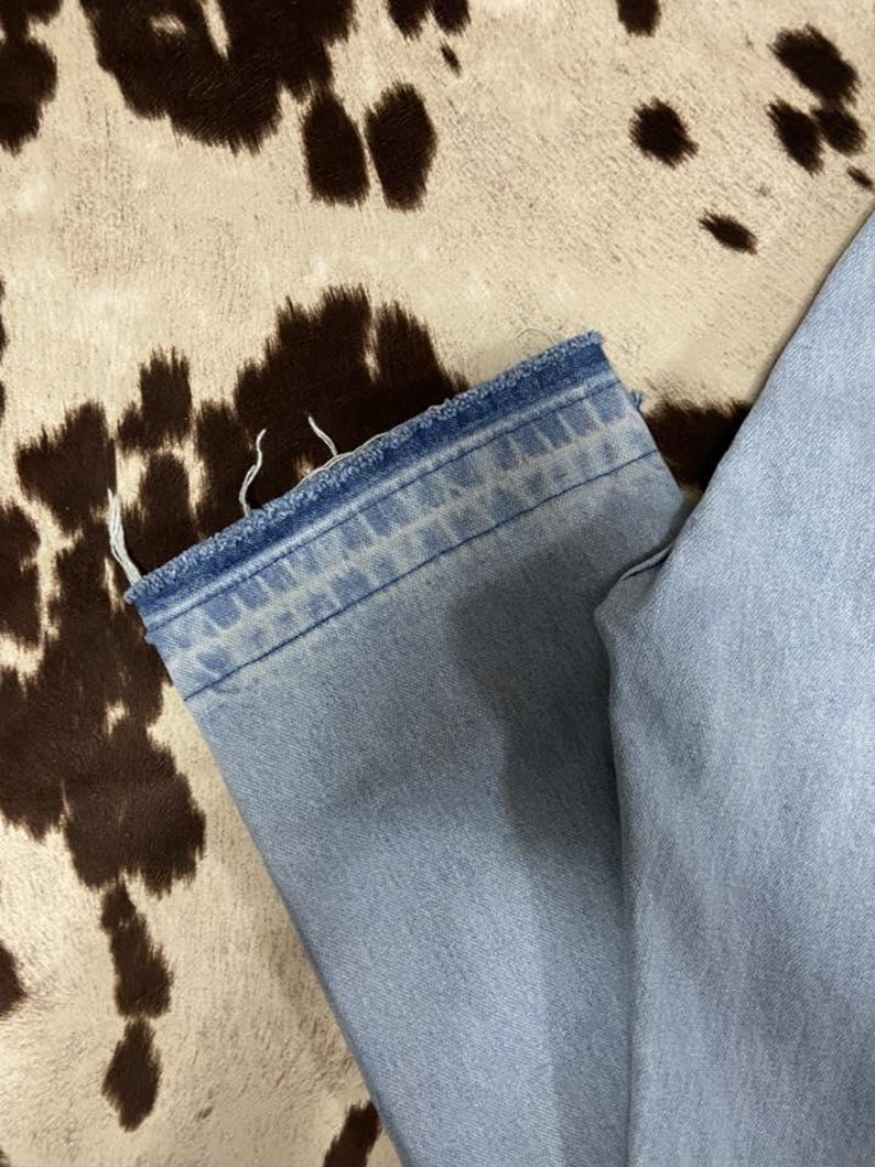 May include: Light blue denim jeans with a frayed hem. The jeans are a light wash. The background is a cowhide pattern in shades of brown and cream.