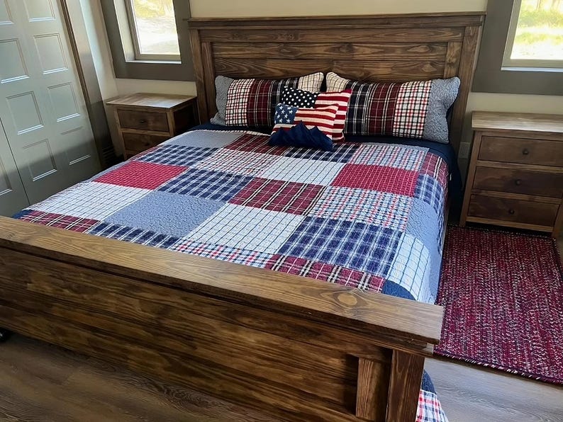 May include: A wooden bed frame with a patchwork quilt in red, white, and blue. The bed is made up with pillows featuring American flag and plaid patterns. A matching rug is on the floor.