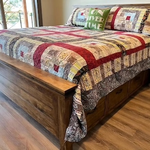 May include: A wooden bed frame with a patterned quilt and matching pillow shams. The quilt features a patchwork design with red, brown, and green squares. A green pillow displays the text "ON RIVER TIME".