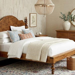 May include: A bedroom set featuring a wooden bed frame, nightstand, and dresser. The bed has a carved headboard and is dressed with white linens and decorative pillows. A beaded chandelier hangs above the bed, and a patterned rug is on the floor.