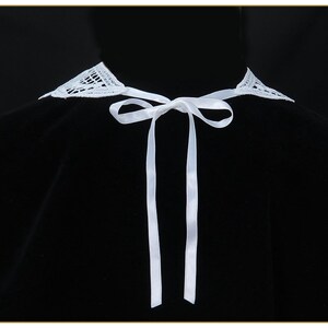 May include: A white lace collar with a white satin ribbon tie. The collar is on a black background.