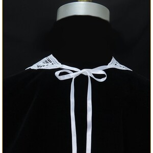 May include: White lace collar with a white satin ribbon tied in a bow. The collar is on a black background.