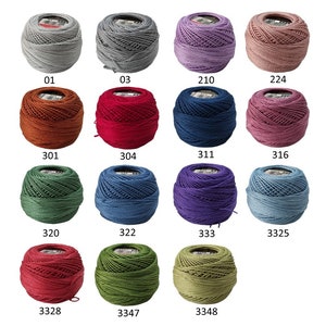Puede incluir: Una colecci&oacute;n de ovillos de hilo coloridos en varios tonos, incluyendo gris, morado, rojo y verde. Cada ovillo tiene una etiqueta con un n&uacute;mero. El hilo parece estar bien enrollado, lo que sugiere que es adecuado para proyectos de artesan&iacute;a detallados.