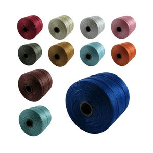 Op de afbeelding: Een verzameling spoelen met gekleurde koorden, waaronder blauw, groen, bruin, rood, oranje, goud en zilver. De spoelen zijn in een cirkel gerangschikt met &eacute;&eacute;n spoel in het midden.