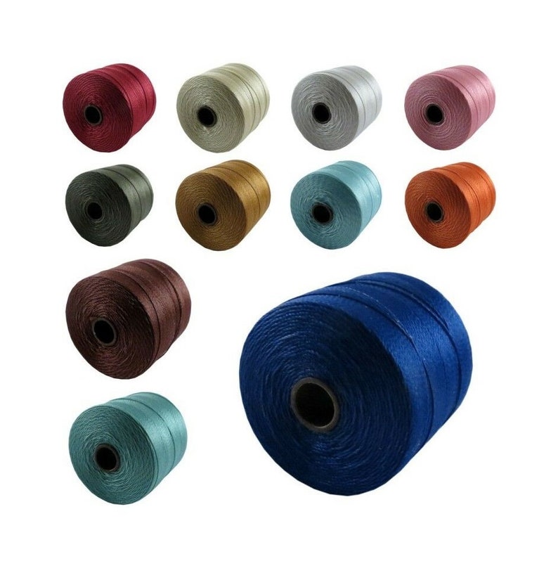 Op de afbeelding: Een verzameling spoelen met gekleurde koorden, waaronder blauw, groen, bruin, rood, oranje, goud en zilver. De spoelen zijn in een cirkel gerangschikt met &eacute;&eacute;n spoel in het midden.