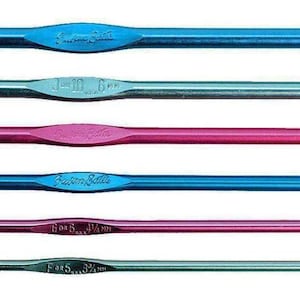 May include: A collection of six crochet hooks in various colors, including blue, pink, and green. The hooks are made of metal and have different sizes, indicated by markings on the shafts. The hooks are designed for yarn crafts.