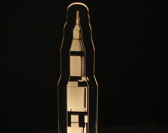 May include: A white acrylic night light shaped like the Saturn V rocket with the text "SATURN 5" at the bottom.