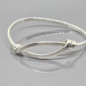 Könnte beinhalten: Ein silbernes Armreif-Armband mit einem verdrehten Knotendesign.