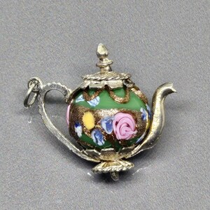 May include: A silver teapot charm with a green, yellow, pink, and blue enamel design. The charm has a floral pattern and a detailed handle.