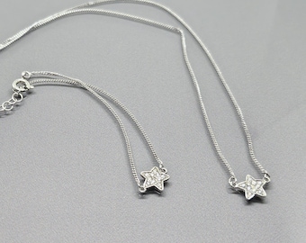 Puede incluir: Dos collares de plata con colgantes en forma de estrella. Cada estrella está incrustada con pequeños cristales transparentes.