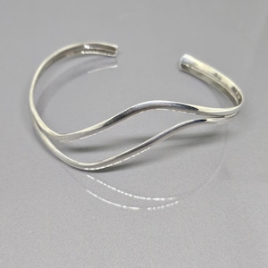 Può includere: Un braccialetto rigido in argento con un design ondulato. Il braccialetto è composto da due sottili bande di metallo intrecciate.