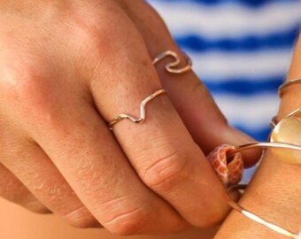 Pode incluir: Pulseiras e anéis dourados adornam um pulso e uma mão. Algumas pulseiras apresentam conchas. O fundo é um padrão de listras azuis e brancas.