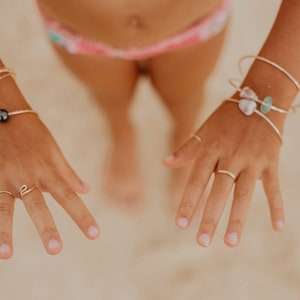 Pode incluir: Close-up das m&atilde;os de uma pessoa usando an&eacute;is e pulseiras de ouro. As pulseiras t&ecirc;m p&eacute;rolas pretas e pequenas pedras. As unhas da pessoa est&atilde;o pintadas de uma cor rosa claro.