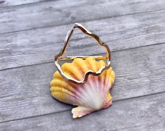Pode incluir: Anel de ouro com um design ondulado abstrato. O anel está apoiado em uma concha de cor amarela e rosa.