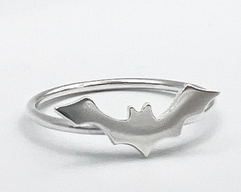 May include: A silver ring with a bat design. The bat is centered on the ring and is facing to the right.
