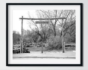 May include: Black and white photograph of a rustic wooden gate with a sign that reads "Texas Nature Trail". The gate is surrounded by trees and bushes.
