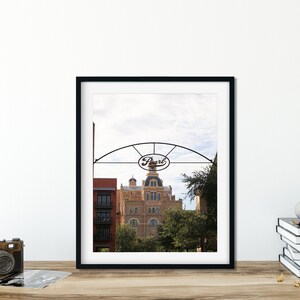 May include: A black framed photograph of a building with a sign that reads "Pearl" above it. The building is a light brown color with a white dome and is surrounded by trees.