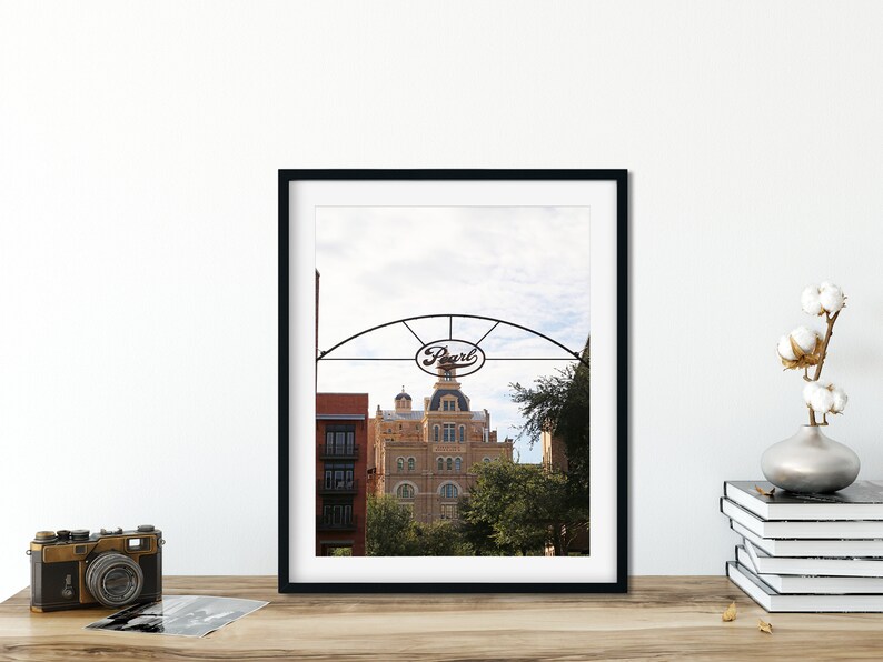 May include: A black framed photograph of a building with a sign that reads "Pearl" above it. The building is a light brown color with a white dome and is surrounded by trees.