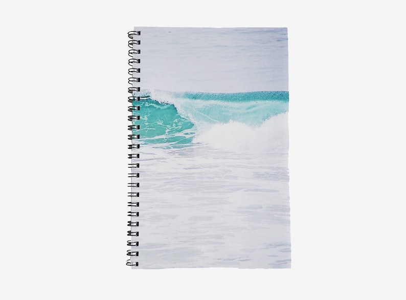 May include: Spiral-bound notebook featuring a vibrant turquoise wave crashing in the ocean. The cover art showcases a detailed depiction of the wave's crest and foamy white water, set against a pale blue sky. The notebook's binding is black.