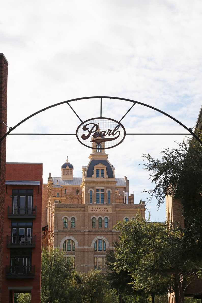 May include: A black metal archway with the word "Pearl" in a white oval sign. The archway is in front of a brick building with a sign that reads "San Antonio Brewery No. 1".