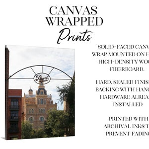 May include: Canvas print of a building with a sign that says "Pearl" above it. The building is a light brown color with many windows. The sign is a black metal arch with the word "Pearl" in white letters. The print is mounted on a hard, high-density wood fiberboard.