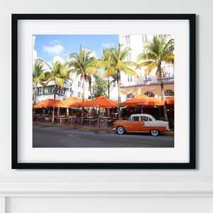 May include: A vintage orange and white car parked in front of a restaurant with orange umbrellas and palm trees.