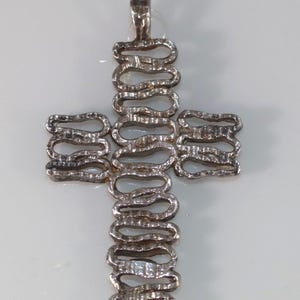 May include: Silver cross pendant with a distinctive design of interconnected loops. The pendant has a textured surface and a loop at the top for a chain. The background is plain white. A unique piece of jewellery.