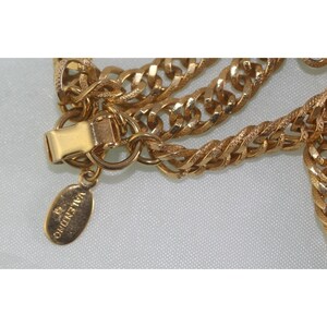 May include: Close-up of a gold-toned chain necklace with a textured curb link design. The necklace features a clasp and a small oval tag with the brand name "VALENTINO" engraved on it. The chain is layered and has a shiny finish.