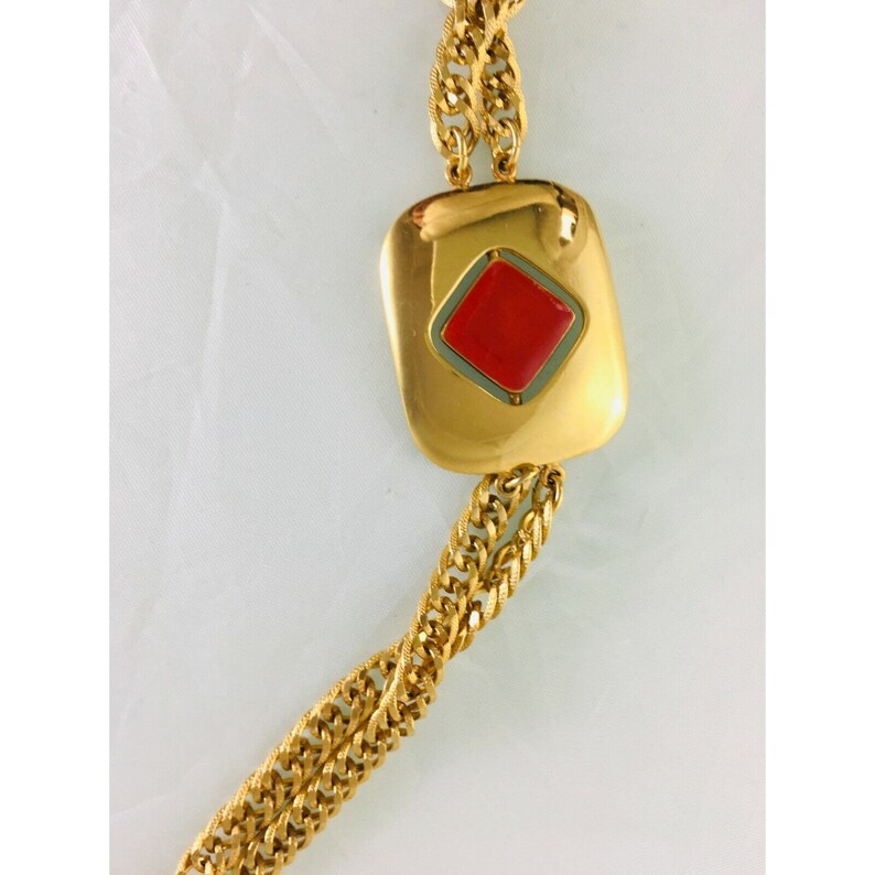 May include: Gold-tone necklace featuring a large, rectangular pendant with a red diamond-shaped center. The pendant is framed by a thin green border. The chain is a thick, textured design. The necklace is displayed against a white background.