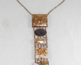 May include: A gold-toned necklace with a chain and pendant design. The pendant features a series of rectangular and oval-shaped elements in shades of brown, gold, and white. Some elements have gold leaf accents. The necklace has a delicate, dangling chain.