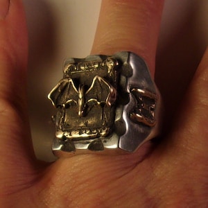 Puede incluir: Anillo de plata con un dise&ntilde;o detallado de murci&eacute;lago en color bronce. El anillo tiene una apariencia texturizada y una est&eacute;tica g&oacute;tica &uacute;nica. El murci&eacute;lago est&aacute; centrado, con las alas extendidas. Una pieza de joyer&iacute;a llamativa.