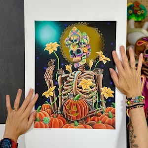 Puede incluir: Una colorida impresión artística con temática del Día de Muertos que presenta un esqueleto con calaveras decoradas, rodeado de calabazas, flores y ratones. La obra de arte tiene un fondo oscuro con una luna dorada y un brillo turquesa.