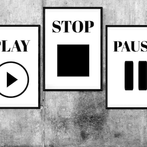 May include: Three black framed signs with white backgrounds and black text. The signs read "PLAY" with a play button, "STOP" with a square, and "PAUSE" with two vertical lines.