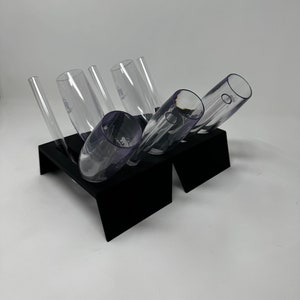 May include: A black acrylic stand with six clear glass champagne flutes. The flutes are arranged in a staggered pattern, with some of the flutes tilted at an angle.