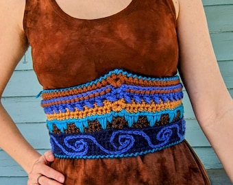 May include: A woman wearing a brown tie-dye dress with a crocheted belt featuring blue, orange, and brown accents. The belt has a geometric pattern with swirls.