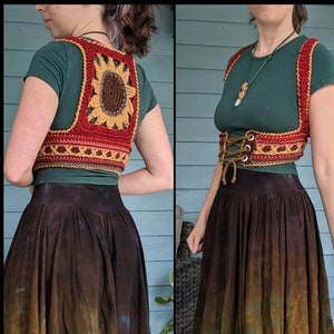 Puede incluir: Una falda marrón y verde con un chaleco de ganchillo de girasol. El chaleco tiene detalles en rojo, amarillo y marrón.