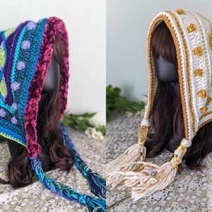 May include: Two crocheted hooded scarves with long tassels. The first scarf is blue, green, and purple with a burgundy velvet trim. The second scarf is white with gold accents.