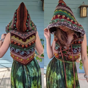 May include: A crocheted vest with a hood, featuring a colourful, geometric pattern with brown, green, and red accents. The vest has a tie closure at the front and is worn over a green and brown tie-dye dress.