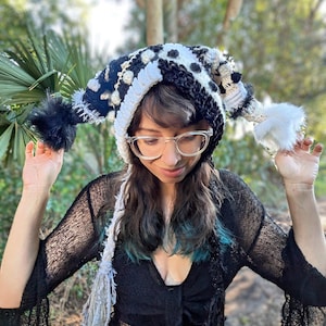 May include: A handmade, whimsical hat with a black and white polka dot pattern, white trim, and fluffy black and white pom-poms. The hat is a unique accessory, perfect for adding a touch of fun to any outfit.