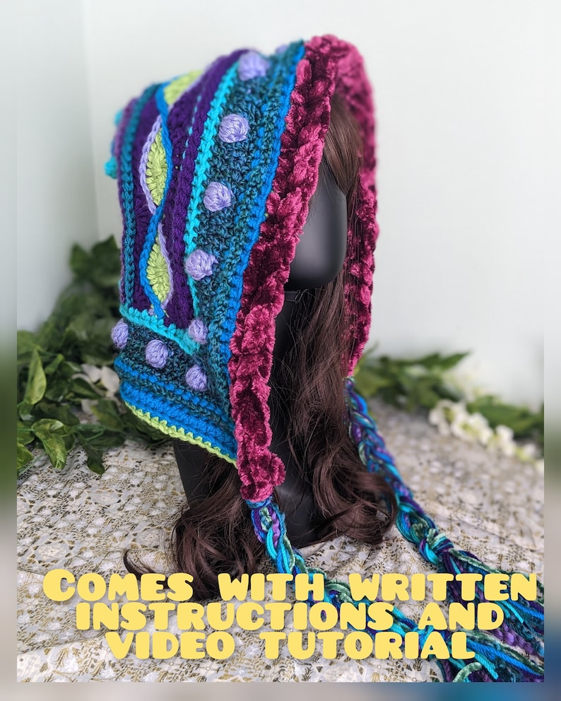 May include: A colorful crocheted hooded scarf with a purple, blue, and green geometric pattern. The scarf has a long, braided tassel and comes with written instructions and a video tutorial.
